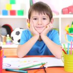 Pensive boy. In front of him is an album and pencils 